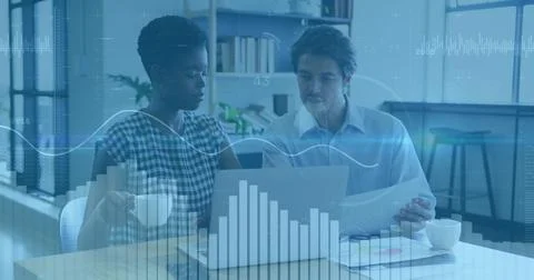Two colleagues analyzing data graphs on laptop while holding printed charts,  Stock Photos
