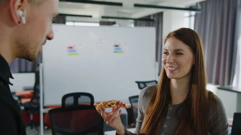 Two colleagues chat during lunch in the office. Woman is holding a pizza Stock Footage 257420522