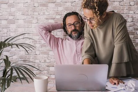 Two colleagues collaborate at a desk, studying laptop and documents while b.. Stock Photos