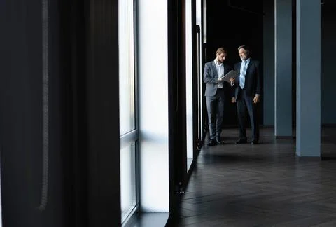 Two colleagues communicating in corridor, partners walking in the modern office Stock Photos