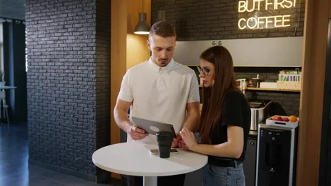 Two colleagues discuss a work project on a tablet in an office cafe Video stock 246052378