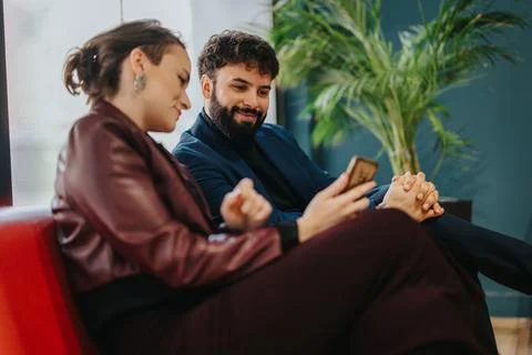 Two colleagues discussing work on a smart phone in a cozy lounge setting Stock Photos