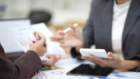 Two colleagues engaged in business analytics, using calculator over financial Stock Footage 280816211