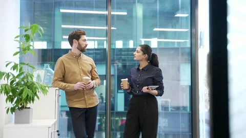 Two colleagues engaged in friendly conversation with coffee in modern office  Stock Footage 309011491