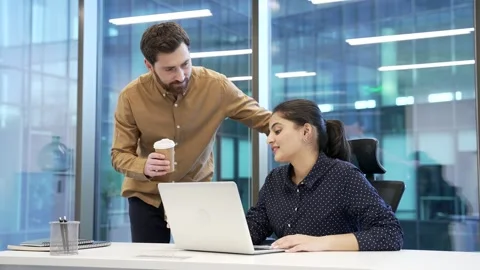 Two colleagues engaged in friendly conversation with coffee at desk at workplace Stock Footage 309011972