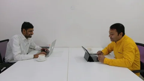 Two colleagues facing each other discuss, argue and smile while working on their Stock Footage 100025734