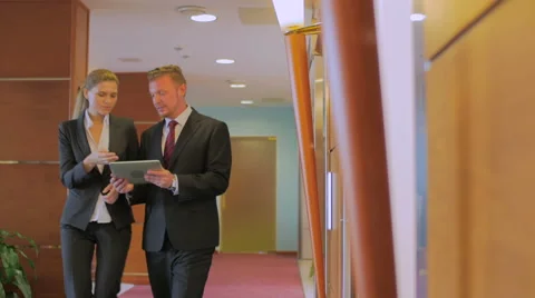 Two colleagues go along the corridor, look in the tablet and discuss the work. Stock Footage 57116565