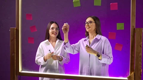 Two colleagues holding markers behind purple sticky note board. Stock Footage 342932894