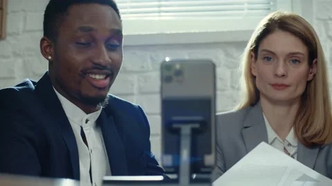 Two colleagues looking at smartphone screen. Smiling African man speaking and Stock Footage 189037703