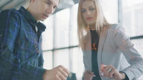 Two colleagues a man and a woman write with a marker formulas and graphs on a Stock Footage 107534853