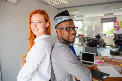 Two colleagues posing smiling in the office back to back, corporate life Stock-Fotos