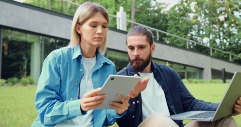 Two colleagues sitting on the grass outdoors, collaborating with a laptop and a  Stock Footage 325733108