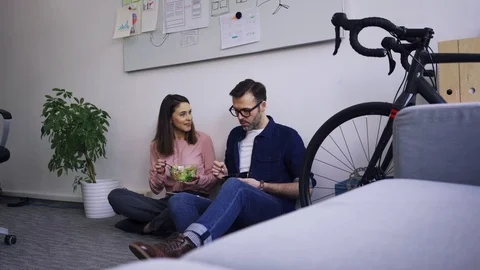 Two colleagues sitting on office floor and having lunch together Stock Footage 102850267