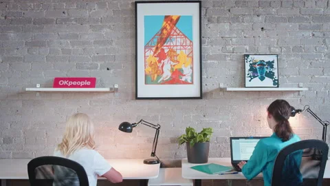 Two colleagues social distance at work while using their electronics, computers, Stock Footage 137042943