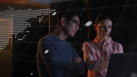 Two colleagues standing in server room, woman tapping laptop, man leaning, Stock Footage 332504797