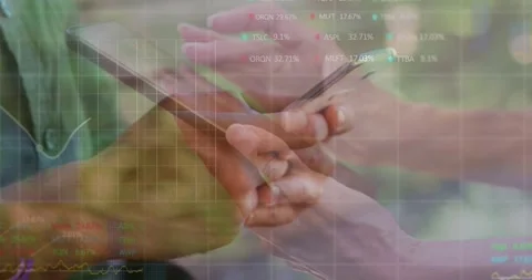 Two colleagues tapping tablet and phone screens, comparing financial charts and Stock Footage 328485675