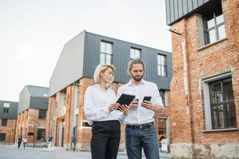 Two colleagues using modern gadgets for work outdoors. Stock Photos
