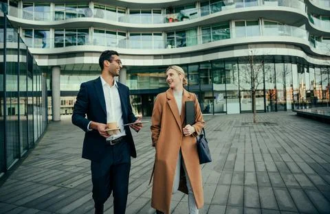 Two colleagues walking together to work discussing meetings while enjoying hot Stock Photos