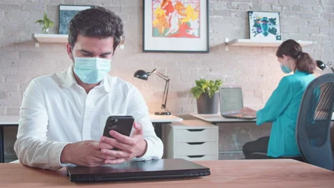 Two colleagues work and social distance while wearing masks and using their Stock Footage 137054289
