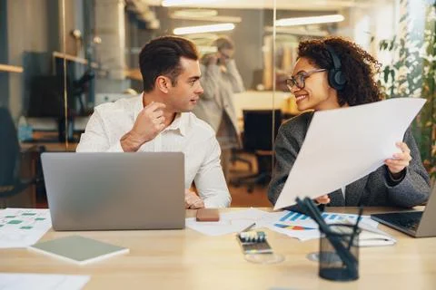 Two colleagues working together with documents while sitting on office desk Stock Photos