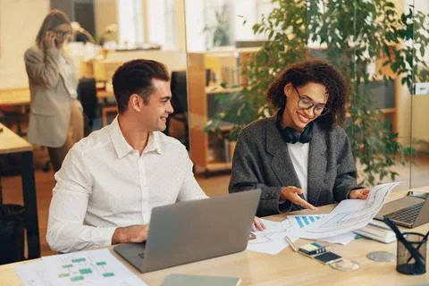 Two colleagues working together with documents while sitting on office desk Stock Photos