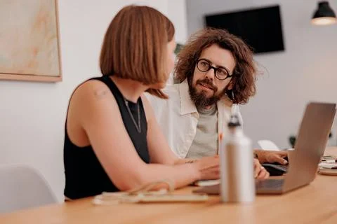 Two colleagues working together on project while sitting on the desk in cozy Stock Photos