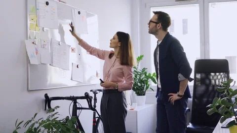 Two colleagues writing on whiteboard while brainstorming in startup hub offic Stock Footage 102858959