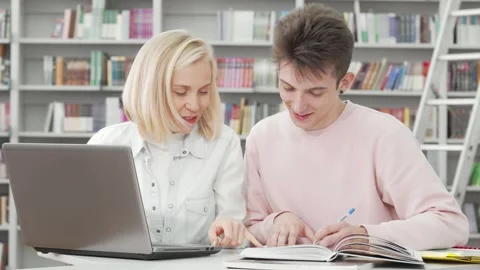 Two college students collaborating on a project in a cozy library Stock Footage 311992824