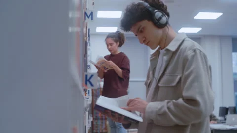 Two College Students Searching for Study Materials Among Library Bookshelves Stock Footage 335127387
