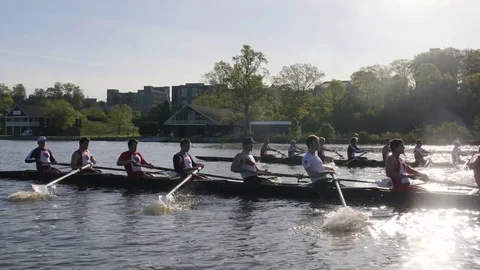 Two collegiate crew boats racing with sun behind them mid boat Stock Footage 80652797