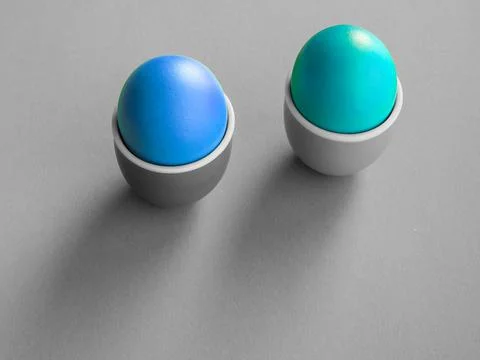 Two colored boiled eggs in ceramic cup or holder on grey background. Stock Photos