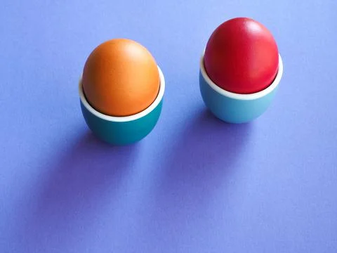 Two colored boiled eggs in ceramic cup or holder on violet background. Stock Photos