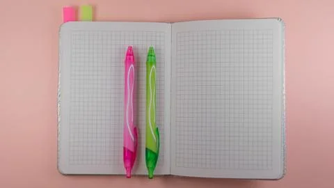 Two colored pens lie on a notebook in a cage Stock Photos