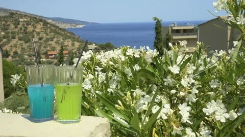 Two colorful drinks on a background of white flowers overlooking the coast Stock Footage 328676690