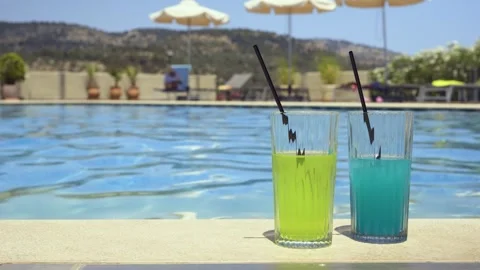 Two colorful drinks beside a pool with umbrellas and mountain view Stock Footage 328671918