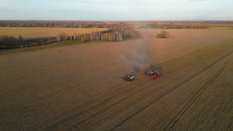 Two combine harvesters work in a field, generating plumes of smoke Stock Footage 289833914
