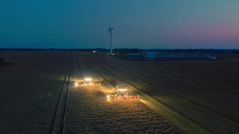 Two combine harvesters working in the blue hours, cutting cereal beside a wind Vídeo Stock 346251084