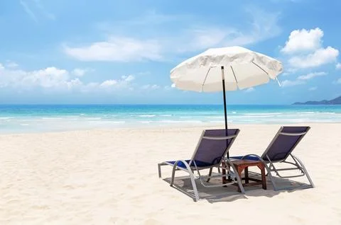Two comfortable beach chairs under a white sun umbrella on a pristine sandy.. Stock Photos
