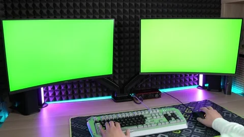 Two computer monitors with green screen mockup. A man typing text Stock Footage 249890587