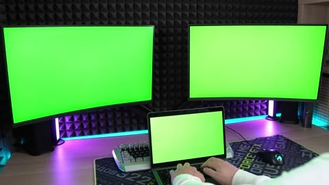 Two computer monitors with green screen and laptop. A man typing text Stock Footage 249890642