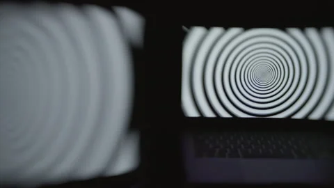 Two computer screens in a dark room displaying a hypnotic spiral pattern. Stock Footage 273038044