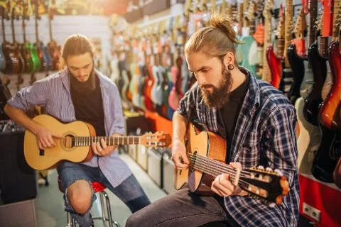Two concentrated young man playing on acoustic guitars. They sit on stools in Stock Photos
