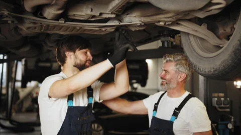 Two confident professional men car mechanic examining car suspension of lifted Stock Footage 243101583