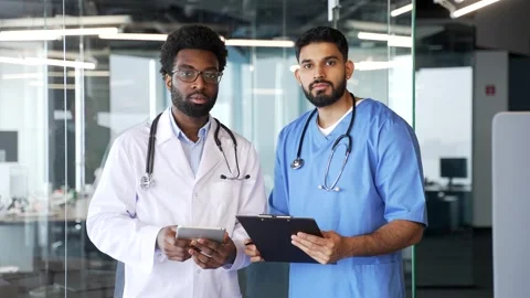 Two confident serious doctors in coats standing indoors in modern hospital Stock Footage 336558189