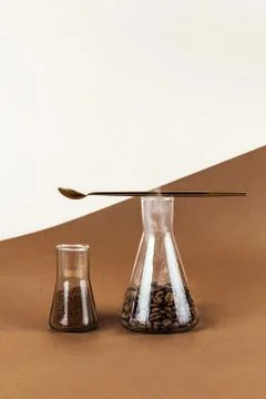 Two conical flasks with groudn coffee and beans on brown and light background Stock Photos