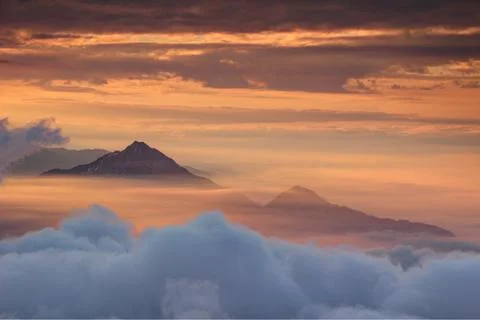 Two conical peaks above translucent autumn morning orange mist Stock Photos