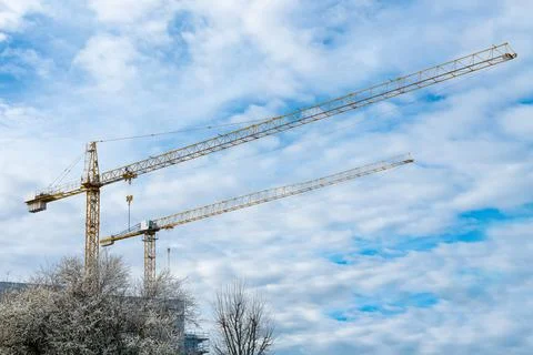 Two construction cranes against a blue sky with light white clouds. Stock Photos