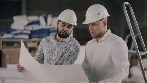 Two construction engineers discuss the architectural plan of the facility at the Video stock 130776295