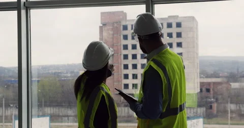 Two construction engineers standing indoors near big window looking at the 库存影片 153170837