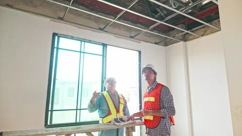 Two construction engineers wearing safety vests and helmets inspect the ceiling Video stock 321448835